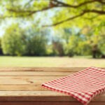 Photo of a park in the summertime with a picnic table featured at the front with a tablecloth.